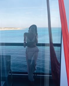 a woman standing on top of a balcony next to the ocean in front of a window