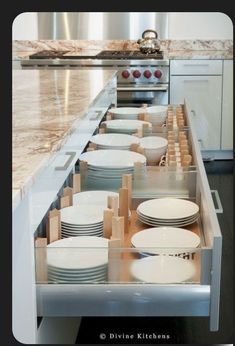 an open drawer in the middle of a kitchen with plates and bowls on it's side