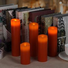 some orange candles are sitting on a table next to books and a cup with saucer