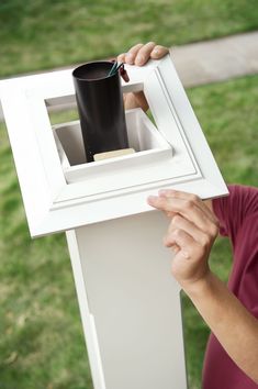 a person holding a cup in front of a white box with a black lid and handle