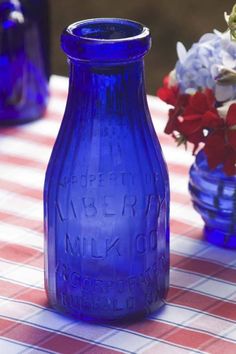 a blue glass bottle sitting on top of a checkered table cloth next to vases filled with flowers