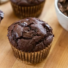 three chocolate muffins sitting on top of a wooden table next to a bowl of chocolate chips