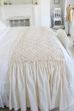 a white bed with ruffled bedspread and pillows