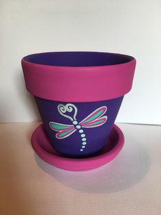 a purple flower pot sitting on top of a saucer with a dragonfly painted on it