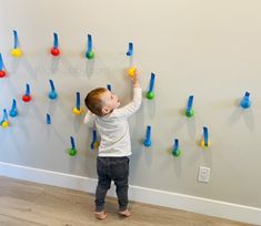 a little boy standing in front of a wall with colorful plastic pegs on it