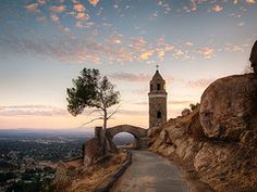 a clock tower sitting on the side of a cliff next to a tree and road