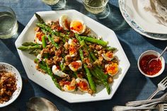 a white plate topped with asparagus covered in hard boiled eggs next to other dishes