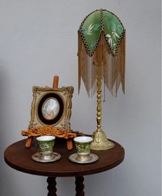 a table topped with two cups and a clock on it's side stand next to a lamp