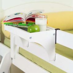 an open book and some books on a white shelf next to a bed with yellow sheets