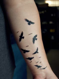 a flock of birds flying across the sky on a person's left arm and wrist