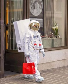 an astronaut walking down the street carrying a shopping bag and wearing a white suit with red accents