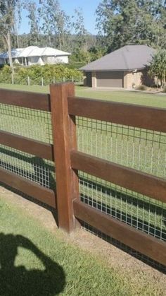 a person standing in front of a fence with grass on the ground and houses in the background