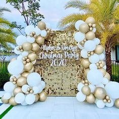 a large white and gold balloon arch with balloons on it in front of a palm tree