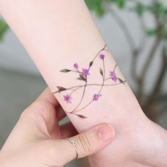 a woman's hand holding a small wrist tattoo with purple flowers on the side