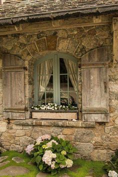 an old stone house with green shutters and flowers in the window sill outside