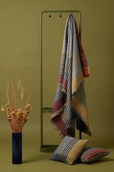 a vase with dried flowers next to a plaid blanket and throw pillows on a stand