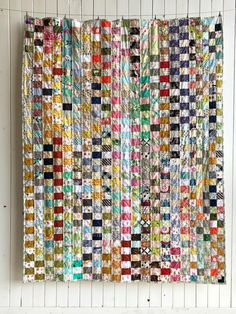 a multicolored quilt hanging on the wall next to a white wooden paneling