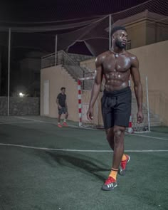 a shirtless man walking across a soccer field at night with his head turned to the side