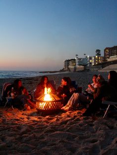 people sitting around a fire pit on the beach