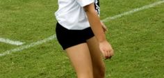 a girl in black shorts and white shirt playing with a red ball on the field