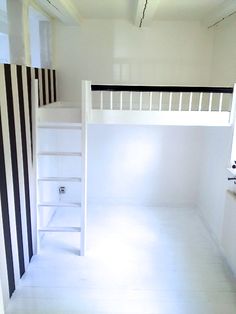 an empty room with black and white stripes on the walls, stairs to the loft bed