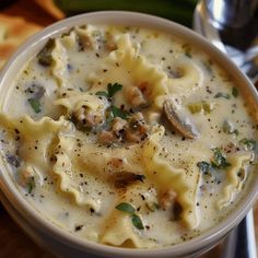 a white bowl filled with pasta and mushrooms on top of a wooden table next to bread