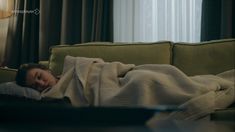 a woman laying on top of a green couch under a blanket