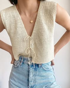 a woman with her hands on her hips wearing jeans and a sleeveless sweater top