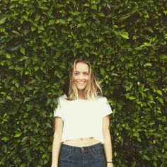 a woman standing in front of a green hedge