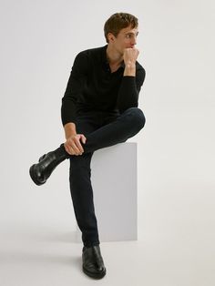 a man sitting on top of a white block with his hand under his chin and looking off to the side