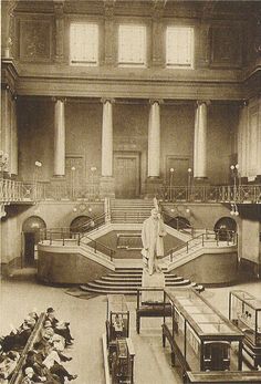 an old black and white photo of the inside of a building with people sitting on benches