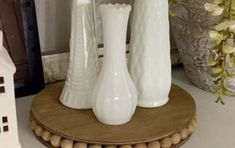 three white vases sitting on top of a wooden stand in front of a clock