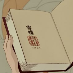 someone holding an open book in their hand with chinese characters on the front and back