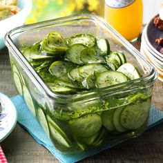 cucumber slices in a glass container on a table with other plates and food