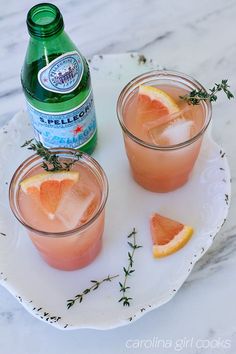 two glasses filled with watermelon and garnish on a plate next to a bottle