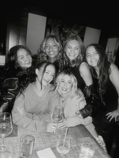 a group of women sitting at a table with wine glasses in front of their faces