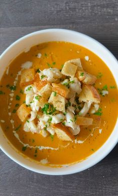 a white bowl filled with soup and croutons on top of a wooden table