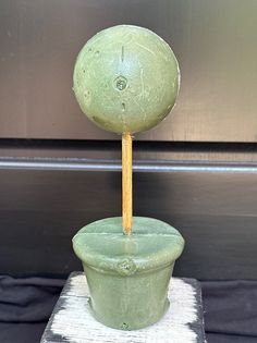 a green vase with a wooden stick sticking out of it's top sitting on a table