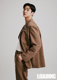 a young man standing in front of a white background wearing a brown jacket and slacks