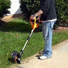 a man using a cordless lawn mower on the sidewalk in front of his house