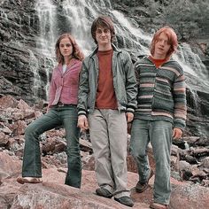 three people standing on rocks in front of a waterfall