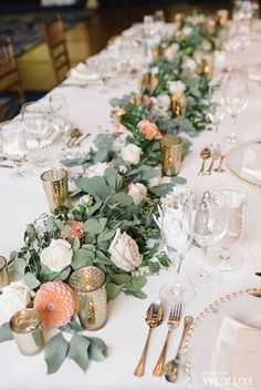 the table is set with white and peach flowers, greenery and gold candlesticks