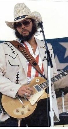 a man in a cowboy hat and sunglasses playing an electric guitar at a music festival