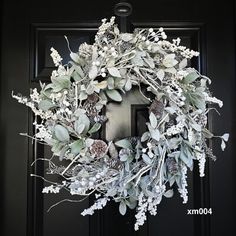 a wreath with white flowers and leaves hanging on a black front door, ready to be decorated for christmas