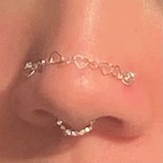 a nose piercing with hearts on it and a chain attached to the side of the nose