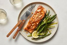 a white plate topped with salmon and green beans next to a glass of water on top of a table