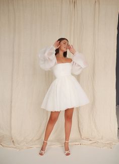 a woman in a white dress posing for the camera with her hands behind her head