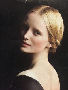 a woman with blonde hair wearing a black dress and looking off to the side, in front of a dark background