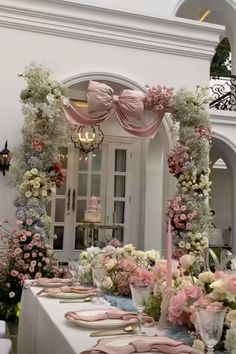 a table set up for a wedding with pink and white flowers on the table, along with plates and napkins