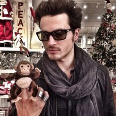 a man holding a monkey in his right hand while wearing sunglasses and a scarf around his neck